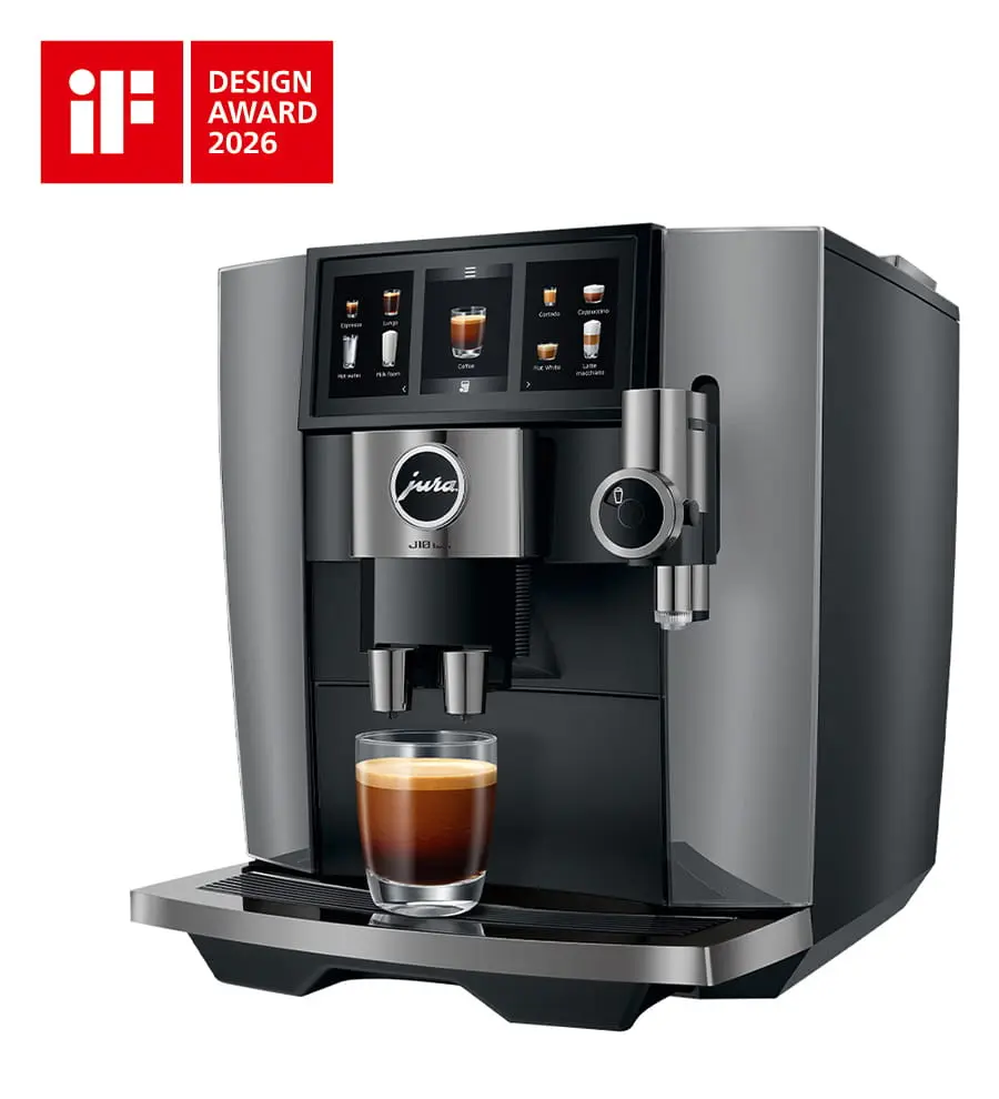Vue de trois quarts droite de la JURA J10 twin Diamond Onyx (SA) préparant un café, avec l'écran Panorama allumé et le mousseur à lait visible. On voit également le logo Design Award 2026 en haut a gauche.